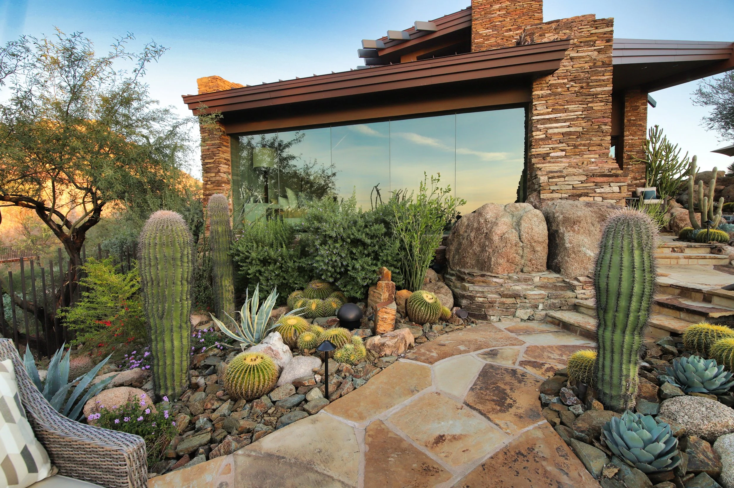 Flagstone walkway lined with barrel cactus, saguaro and boulders beside a stone home